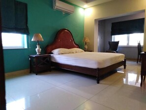 A bedroom with a wooden bed, two bedside tables with lamps, a window with a curtain, and a door leading to another room. - Morgah Resort Villas (Rawalpindi)