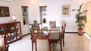 Uma área de refeições com mesa e cadeiras de madeira, um armário de vidro com louças e um vaso com planta.