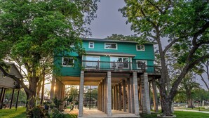 A two-story house with a balcony, supported by columns, surrounded by trees. - Turtle House-Pool Table-Shuffle Board-5 Bedrooms-Sleeps 12! (Seguin)