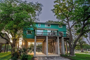 A two-story house with a balcony, supported by columns, surrounded by trees.