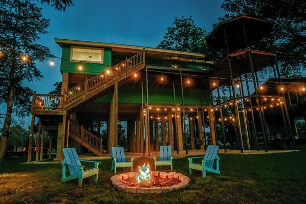 A two-story wooden structure with a deck, outdoor seating, and a fire pit.