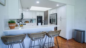 A modern kitchen with white cabinets, a central island, bar stools, and a stainless steel refrigerator. - Turtle House-Pool Table-Shuffle Board-5 Bedrooms-Sleeps 12! (Seguin)