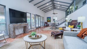 A spacious living area with a fireplace, a flat-screen TV, and a dining area with a staircase leading to an upper level. - Turtle House-Pool Table-Shuffle Board-5 Bedrooms-Sleeps 12! (Seguin)