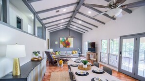 A spacious dining area with a high ceiling and exposed beams, a large window, and a modern kitchen in the background. - Turtle House-Pool Table-Shuffle Board-5 Bedrooms-Sleeps 12! (Seguin)
