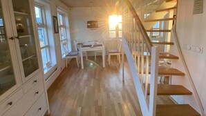 A spacious room with a wooden floor, a dining area with a table and chairs, and a staircase with a wooden railing.