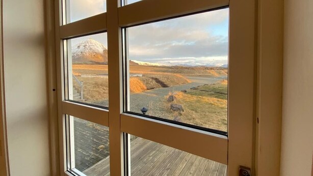 A view through a window with a wooden deck and a mountainous landscape.