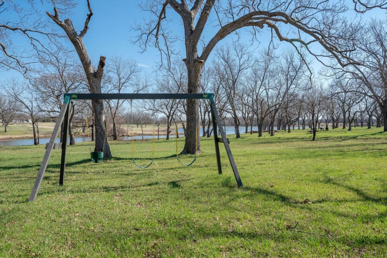 A swing set in a park with trees and a body of water in the background.