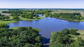 A large body of water surrounded by dense green trees and open fields.