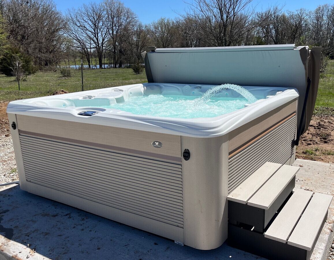 Un jacuzzi con terraza de madera y estructura metálica, ubicado al aire libre con árboles en el fondo.