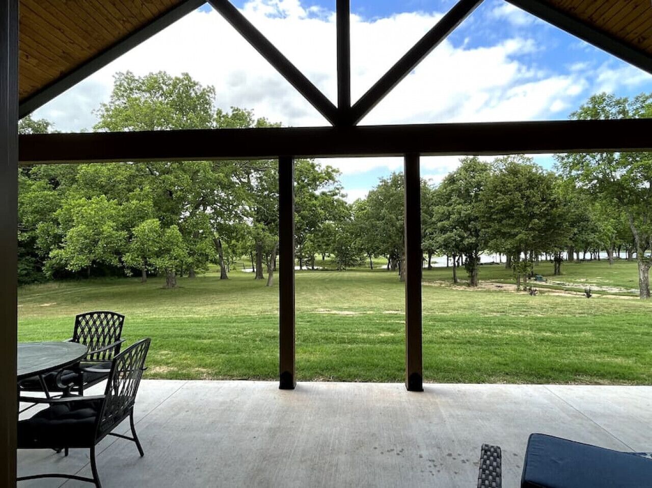 A covered patio with a table and chairs, overlooking a grassy park area with trees.