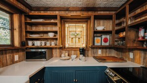 Een keuken met houten kastjes, een magnetron, een koffiezetapparaat en een groot raam.