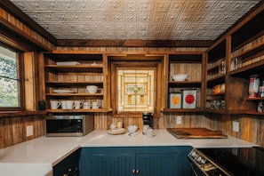 Compact kitchen with a stove, sink, and coffee maker, featuring cabinetry and a countertop.