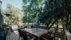 Een terras buiten met een houten tafel en stoelen, een parasol en een ingebouwde bank.