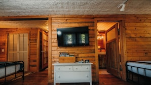 Interieur van een blokhut met een televisie aan de wand, een witte dressoir en een gestreept vloerkleed.