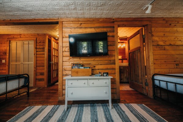 A log cabin interior with a television mounted on the wall, a white dresser, and a striped rug on the floor.
