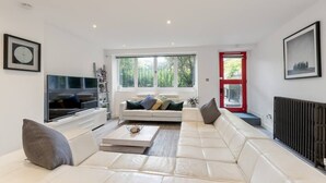 A modern living room with a large white sofa, a flat-screen TV, and a red-framed door. - Luxury Architect Designed Apt 13 Mins 2 Royalmile❤ (Edinburgh)