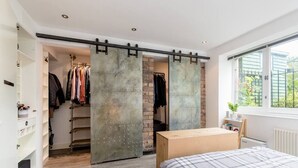A bedroom with a sliding closet door, a bed with a plaid duvet, and a window with a view of greenery. - Luxury Architect Designed Apt 13 Mins 2 Royalmile❤ (Edinburgh)