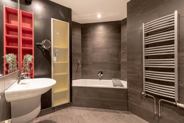 A modern bathroom with a white sink, a bathtub, and a towel rack.