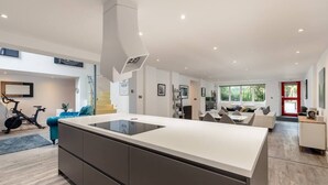 A modern kitchen with a central island, a dining area with a sofa, and a visible exercise bike. - Luxury Architect Designed Apt 13 Mins 2 Royalmile❤ (Edinburgh)