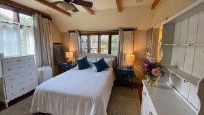 Een slaapkamer met een groot bed, twee nachtkastjes met lampen, een plafondventilator en een witte dressoir.