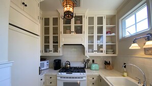 Een keuken met witte kastjes, een fornuis, een magnetron, een spoelbak en een raam met natuurlijk licht.