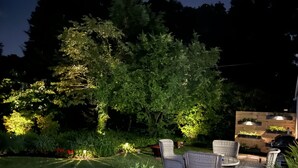 Eine Terrasse mit Korbmöbeln, einem runden Tisch und einem Blumentopf mit roten Blüten.