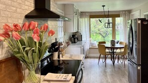 Eine moderne Küche mit einer schwarzen Dunstabzugshaube, weißen Schränken, einem Esstisch mit Stühlen und einer Vase mit rosafarbenen Tulpen auf der Arbeitsfläche.