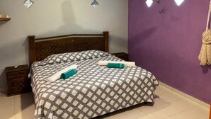 Een slaapkamer met een bed, een plafondventilator, een airconditioner en een paarse wand.