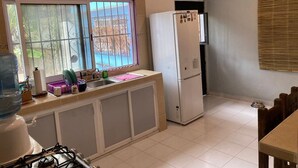 Een kleine keuken met een koelkast, een spoelbak en een raam met tralies.