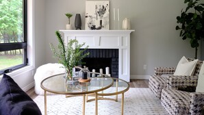 Una sala de estar con chimenea, una mesa redonda de vidrio y un sofá estampado.