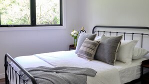 Una cama bien hecha con una colcha gris, cabecero de metal negro y una alfombra estampada.