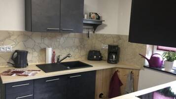A kitchen with dark cabinets, a marble backsplash, a coffee maker, and a kettle.