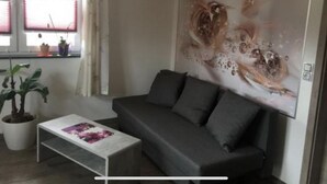 A living room with a grey sofa, a coffee table with a magazine, a large abstract painting on the wall, and a window with curtains.