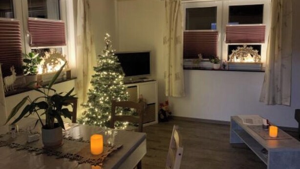 A cozy living room with a Christmas tree, a television, and a dining table with candles.