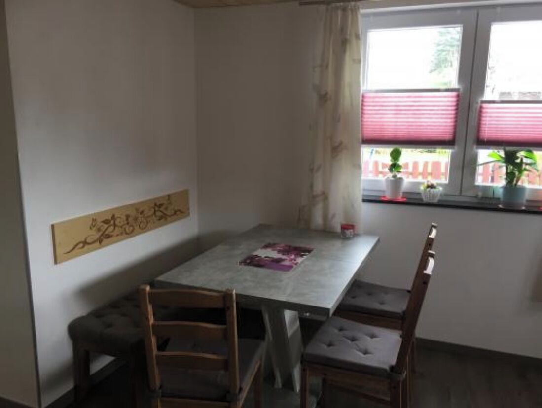 Ein Essbereich mit Tisch und vier Stühlen, einer Wandverkleidung und einem Fenster mit Jalousien und Topfpflanzen.