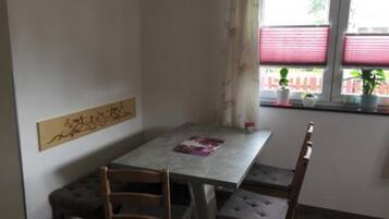 Ein Essbereich mit Tisch und vier Stühlen, einer Wandverkleidung und einem Fenster mit Jalousien und Topfpflanzen.