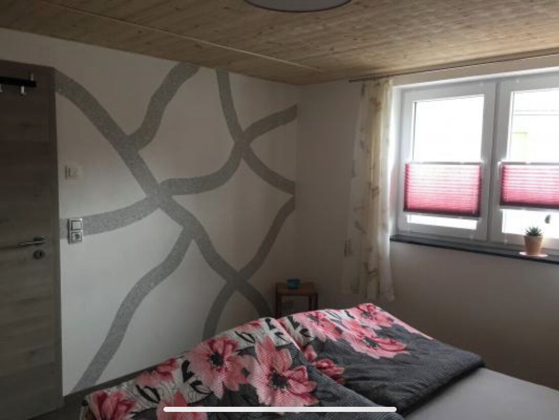 A bedroom with a bed, a window with blinds, and a wall with a geometric pattern.
