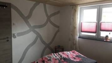 A bedroom with a bed, a window with blinds, and a wall with a geometric pattern.