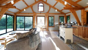 Un'ampia stanza con soffitto alto, travi in legno, una grande finestra, un divano, un tavolo da pranzo e un angolo cottura.
