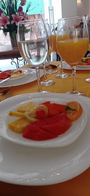 A table with a white plate of fruit, two glasses of water, and a glass of orange juice.