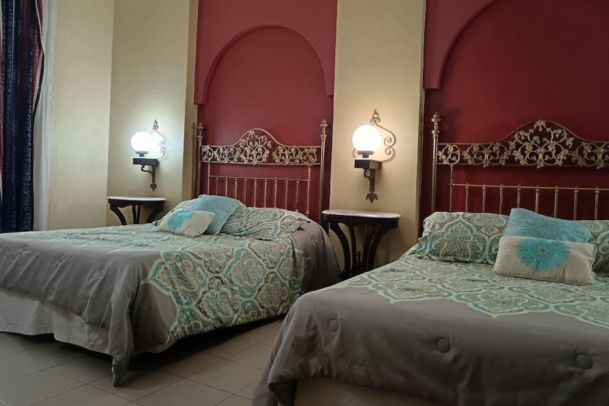 Two single beds with headboards, bedside tables, and wall-mounted lamps in a room with red arches on the walls.