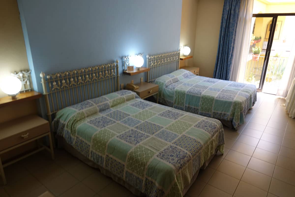 A hotel room with two beds, bedside tables, and a view of the outside.