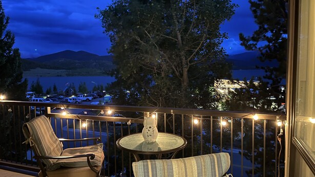 A balcony with two chairs and a table, overlooking a lake and mountains at dusk. - Summit Serenity: Luxury Alpine Ski Escape in Dillon, CO (Dillon)