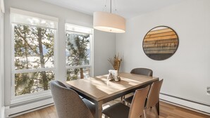 A dining area with a wooden table, four chairs, a hanging light fixture, and a wall-mounted circular artwork. - Summit Serenity: Luxury Alpine Ski Escape in Dillon, CO (Dillon)