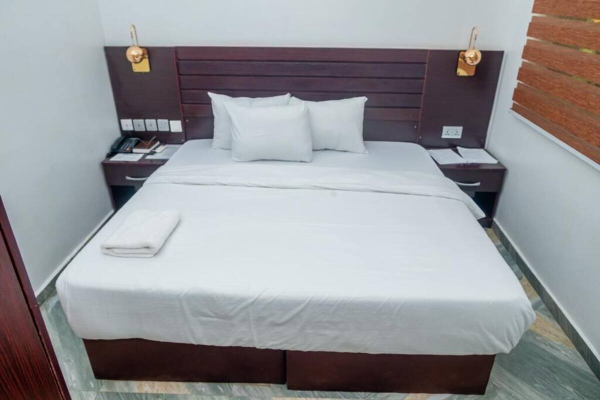 A neatly made bed with white linens, a wooden headboard, bedside tables with lamps, and a small nightstand with a phone and papers.