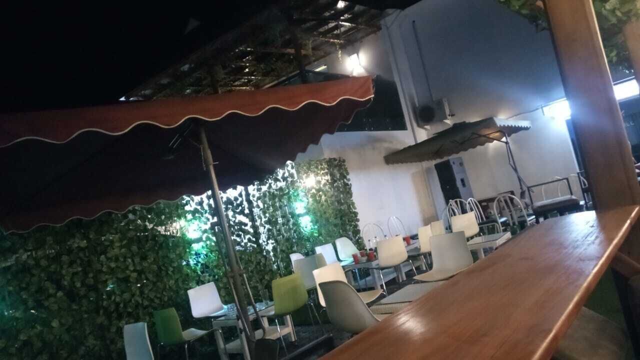 Un área de comedor al aire libre con una mesa y sillas de madera, un toldo rojo y una pared adornada con follaje.