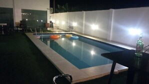 Piscina com borda azulejada, rodeada por um muro branco e um pequeno espaço com espreguiçadeiras.