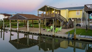 A waterfront property with a covered deck, outdoor seating, and a dock extending into a calm body of water.