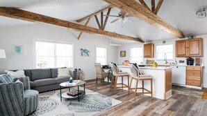 A spacious living area with a gray sofa, wicker chairs, a coffee table, and a kitchen with wooden cabinets and a bar area.