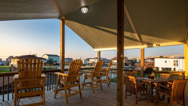 A wooden deck with chairs and tables, overlooking a body of water and buildings.